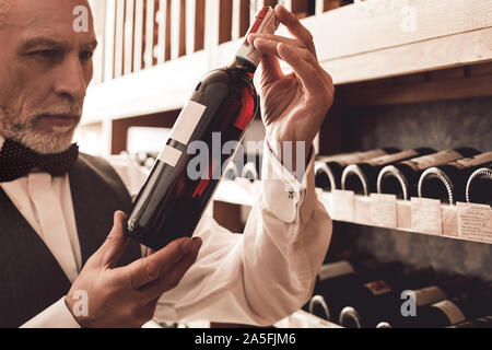 Sommelier Concept. Senior man standing with bottle of wine pensive close-up Stock Photo