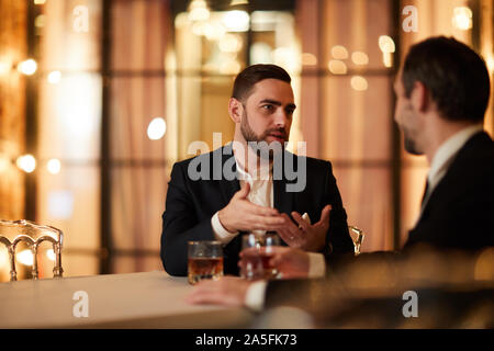 Portrait of two business people talking while sitting at table in luxury restaurant and drinking alcohol after work, copy space