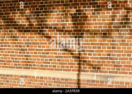 Reddish brown brick wall texture with English bond brickwork pattern, showing shadows from trees and a street light Stock Photo