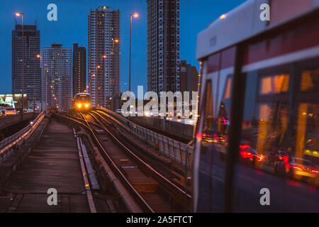 Bangkok, Thailand - June 25, 2019: a BTS train arrives in Saphan Taksin station at night. High-rise buildings of Khlong Ton Sai, Khlong San. Stock Photo