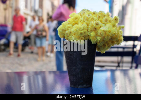 chrysanthemums yellow blossom stands in black pot on table. People walking in the background Stock Photo
