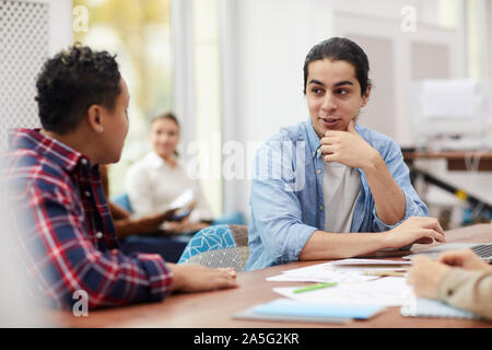 Group of students studying together in library, focus on Latin-American man sharing ideas with team, copy space Stock Photo