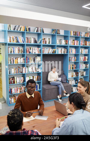 Wide angle view at multi-ethnic group of students studying in modern library of university or college, copy space Stock Photo