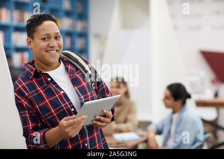 Waist up portrait of smiling Latin-American college student looking at camera while standing in modern library, copy space Stock Photo