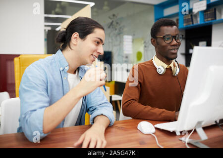 Portrait of two smiling college students using computer while researching for project in library, copy space Stock Photo