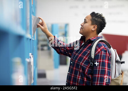 Side view portrait of mixed-race woman choosing books standing by shelves in college library, copy space Stock Photo