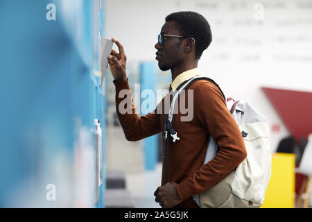 Side view portrait of African-American student choosing books standing by shelves in college library, copy space Stock Photo