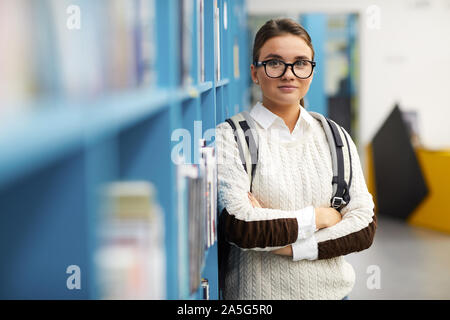 Waist up portrait of young freshman looking at camera while standing by shelves in college library, copy space Stock Photo