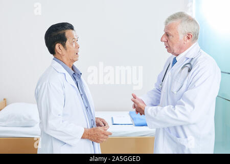 Serious multi-ethnic senior doctors in white lab coats discussing difficult cases in work Stock Photo