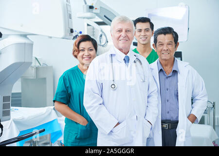 Smiling multi-ethnic group of doctors and surgeons standing in operating room of hospital Stock Photo