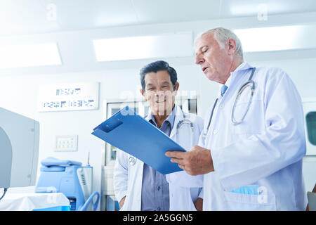 Doctor showing medical history of patient to his Vietnamese coworker and asking for advice Stock Photo