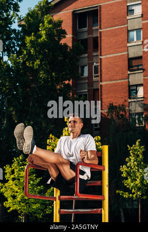 Young muscular build man doing dips exercises on horizontal bar outdoors Stock Photo