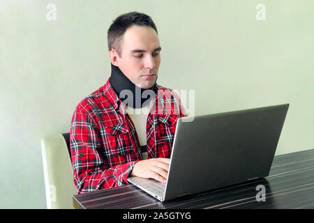 Man freelancer in a cervical collar neck brace working from home. neck support on the prosthesis. fracture of the cervical vertebrae. Treatment of nec Stock Photo