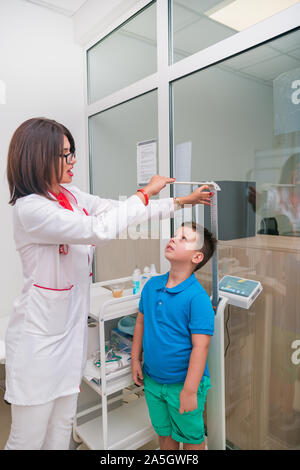Female doctor measuring the height of little boy in a clinic ( hospital ) while smiling and being gentle. Stock Photo