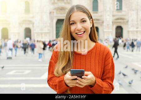 Happy young woman with sweater at good news on her mobile phone looking at camera on city square. Stock Photo