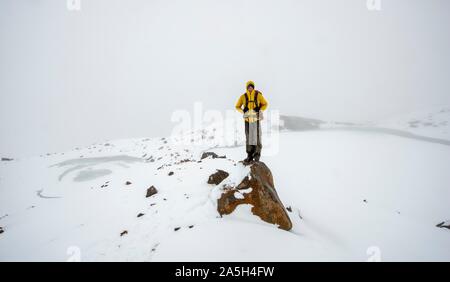 Hiker standing on stone, Emerald Lake Lookout in snow, Frozen Emerald Lakes, Tongariro Alpine Crossing, Tongariro National Park, South Island, New Stock Photo