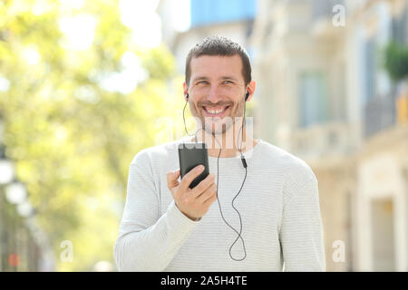 Front view portrait of a happy adult man listening to music looking away in the street Stock Photo