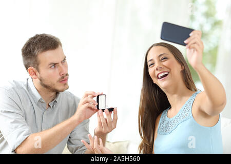 Upset man proposing marriage and girlfriend taking selfie sitting on a couch at home Stock Photo