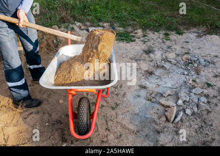 worker pours sand into a wheelbarrow Stock Photo