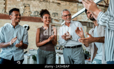 Congratulations! Multicultural team clapping their hands and smiling while standing in the creative office Stock Photo