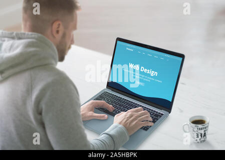 Web designer works on a promo website concept. Office desk, close-up. Flat design web site on laptop screen. Stock Photo
