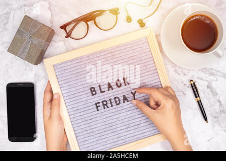 word Black Friday on letter board on white marble desk background with coffee cup ,gift box and smart phone with blank screen Stock Photo