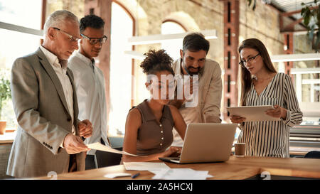 Project team. Multicultural team looking at the laptop and discussing project results while working together in the modern office Stock Photo