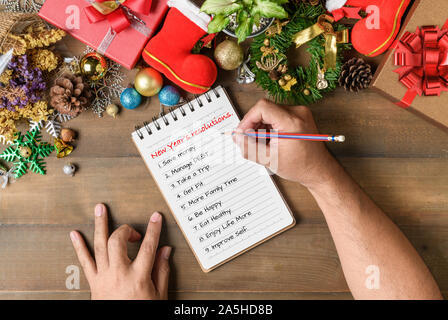 Hand man writing New year resolution on note paper with decorations and gift boxes, New year and Merry christmas goal  conceptual Stock Photo