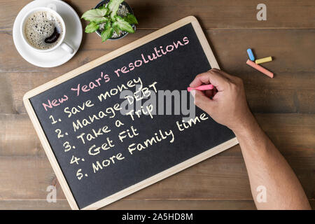 Hand man writing New year resolution on black board with coffee and wood background, New year goal  conceptual Stock Photo