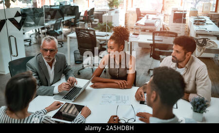 Business meeting. Mature man in formal wear discussing something with coworkers while sitting together at the office table Stock Photo