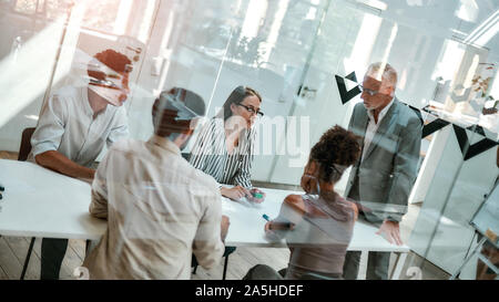 Morning meeting. Group of business people discussing something while sitting at the office table behind the glass wall in the modern office Stock Photo