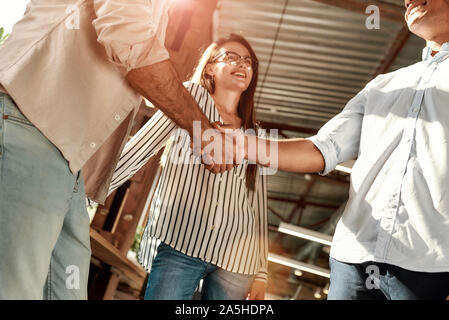Hello! Two men shaking hands and smiling while standing with coworkers in the modern office Stock Photo
