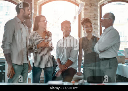 Positive team. Group of cheerful business people discussing something and smiling while standing in the modern office Stock Photo
