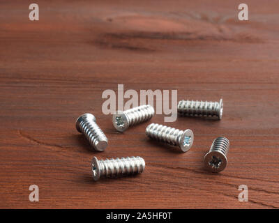 Set of silver color steel screws on a brown wooden background Stock Photo