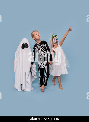 Three kids in Halloween costumes holding hands over blue background Stock Photo