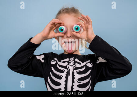 Little boy in skeleton costume holding scary toy eyeballs over his eyelids Stock Photo