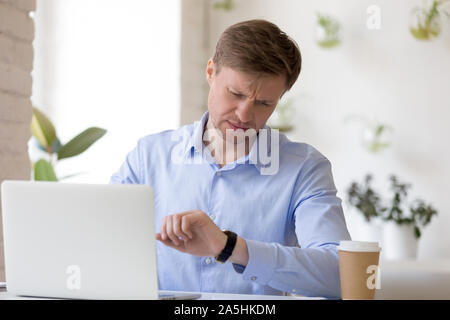 Frowning middle aged entrepreneur looking at wristwatch, waiting for partners. Stock Photo