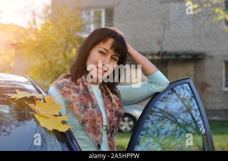 Attractive young woman near her car in the fall. A rich adult female by the car. Confident woman. Stock Photo