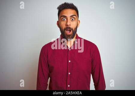 Young indian man wearing red elegant shirt standing over isolated grey background afraid and shocked with surprise and amazed expression, fear and exc Stock Photo