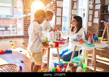 Beautiful teacher and toddlers playing cooking with plastic food around lots of toys at kindergarten Stock Photo