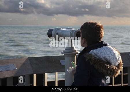 Young child looking out through binoculars on Hastings pier in daytime Stock Photo