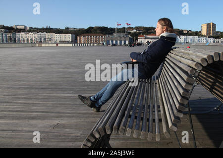 Woman sitting on wooden bench on Hastings pier relaxing with eyes closed in the cool breeze, from side, daytime 2019, with copy space Stock Photo