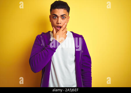 Young brazilian man wearing purple sweatshirt standing over isolated yellow background Looking fascinated with disbelief, surprise and amazed expressi Stock Photo