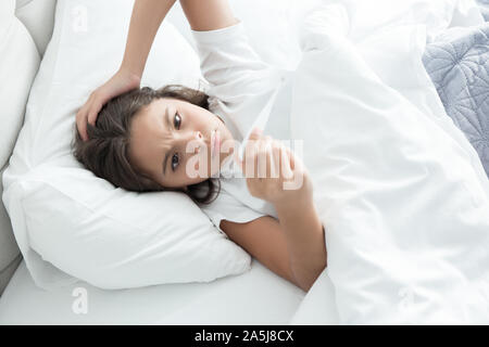 cute teen girl lying in bed with termometer in her hand Stock Photo