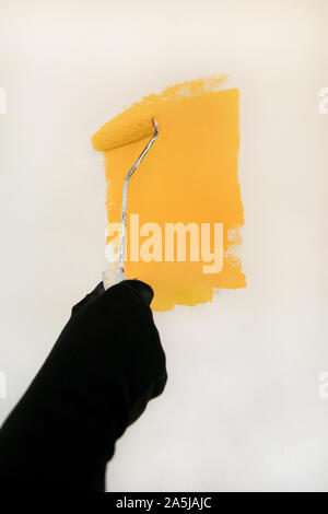 Construction worker doing finish renovation at apartment. Professional painter using paint roller brush painting of wall with yellow color. Stock Photo