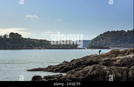 A lone fisherman at Rusty Anchor on Plymouth’s waterfront, sets up his tackle. In the distance the historic Drake’s Island ready for redevelopment and Stock Photo