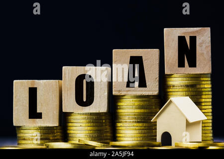 Saving money, home loan, mortgage, a property investment for future concept. A wooden block on stacked of coins with a small residence house on dark b Stock Photo