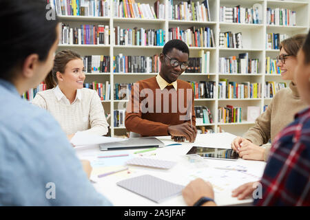 Multi-ethnic group of students sharing ideas while discussing team project during meeting in college library, copy space Stock Photo