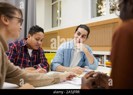 Multi-ethnic group of students discussing group project and brainstorming ideas while sitting at desk in college library, copy space Stock Photo