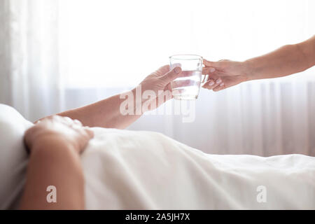 A nursing home worker holds out a mug of water to an elderly woman. The concept of care for the elderly and rehabilitation in a boarding house, close- Stock Photo
